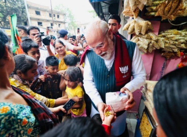 PM Modi holding a cup of jhalmuri amid an enthusiastic crowd at the Jhargram stall, embodying his approachable style during the campaign.